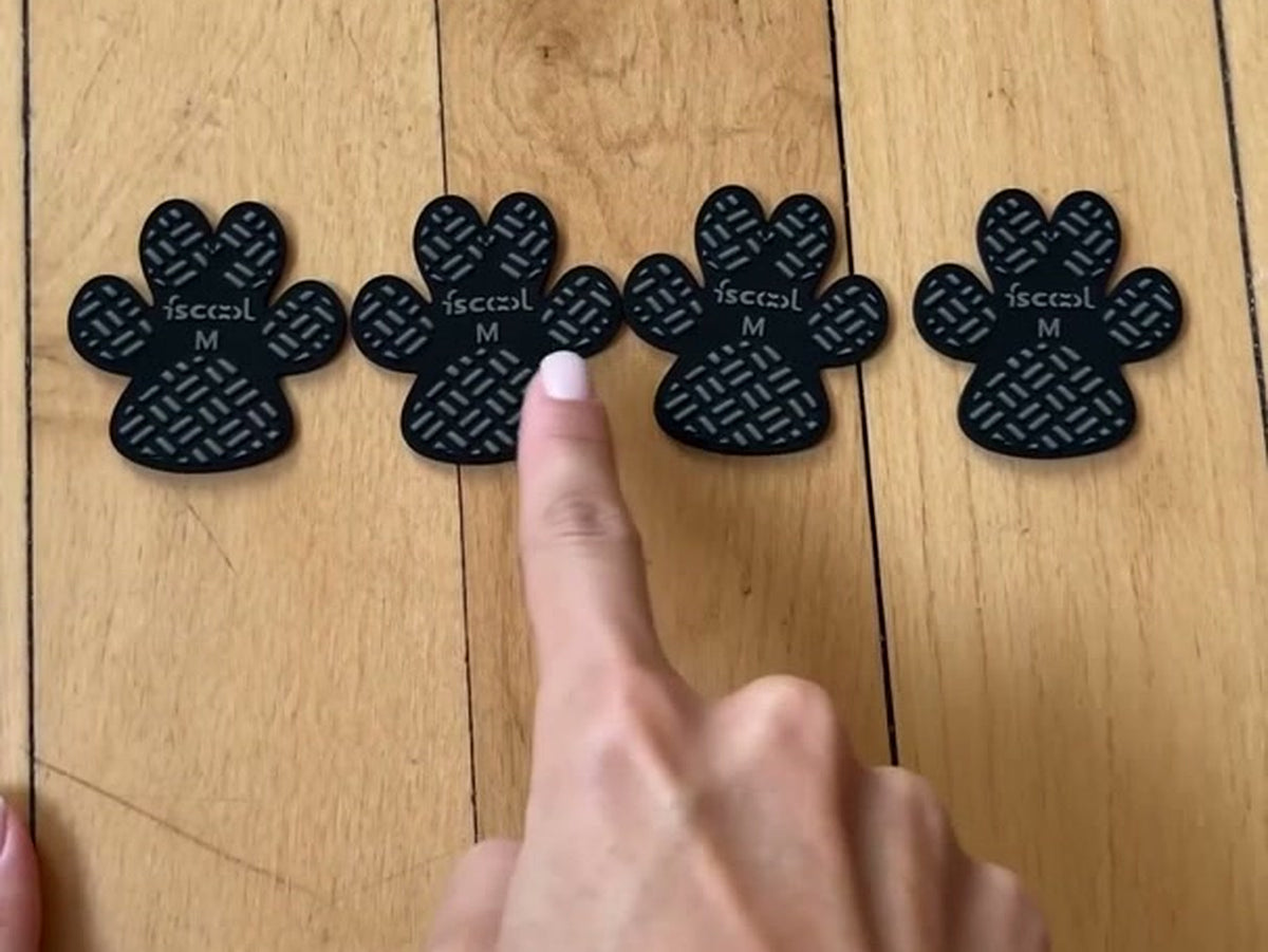 Four anti-slip paw grips laid out on a wood floor next to a hand