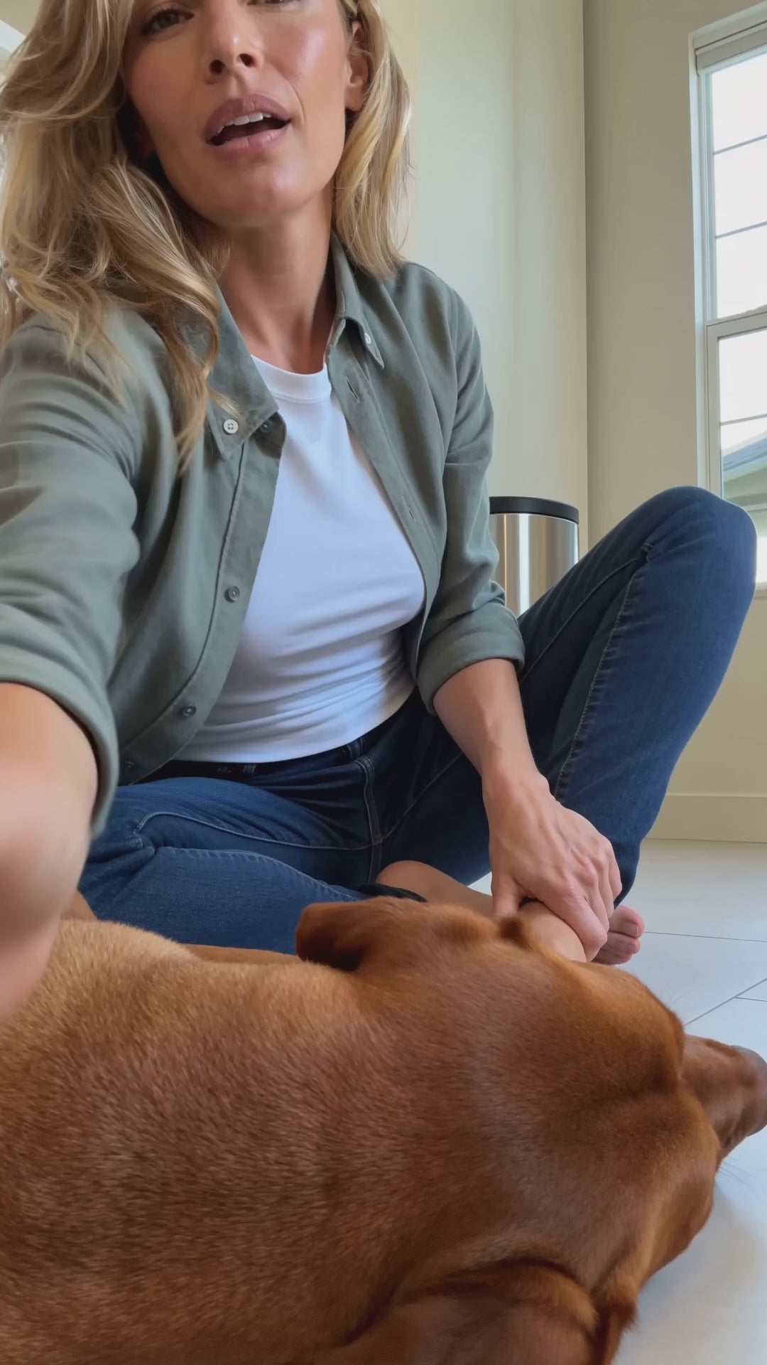 A woman sits on her kitchen floor with her dog and uses the quiet nail grinder, taking a little off at a time